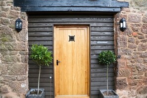 A wooden door with a small window, flanked by two potted plants. - Muddifords Court (Tiverton)