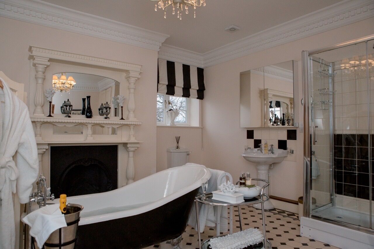 Ein klassisches Badezimmer mit freistehender Badewanne, einer Glasdusche, einem weißen Waschbecken und einem Spiegel darüber.