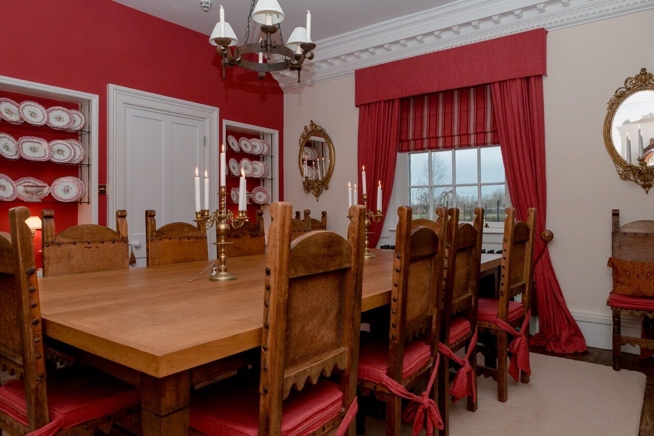 Une salle à manger avec une table et des chaises en bois, des rideaux rouges et un lustre.
