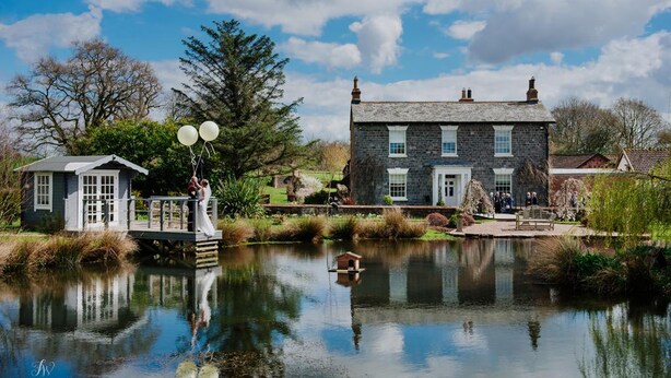 A stone house with a pond in front, a wooden bridge, and a gazebo. - Muddifords Court (Tiverton)