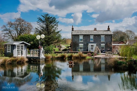 A stone house with a pond in front, a wooden bridge, and a gazebo.