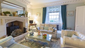 A traditional living room with a fireplace, comfortable seating, and a large window with curtains. - Muddifords Court (Tiverton)