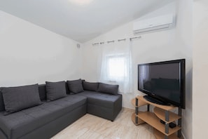 Una sala moderna con un sofá modular, un televisor de pantalla plana sobre un soporte de madera y un equipo de aire acondicionado en la pared.