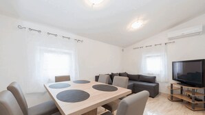 A modern living room with a wooden dining table, grey sofas, and a flat-screen TV. - Apartment Banic (Vir)