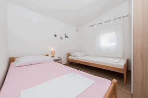 Un dormitorio con dos camas individuales, una mesita de noche con lámpara y una ventana con cortinas.