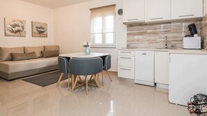 A modern kitchen with white cabinets, a dining table with chairs, a sofa, and artwork on the wall. - Apartments Kosic (Vir)