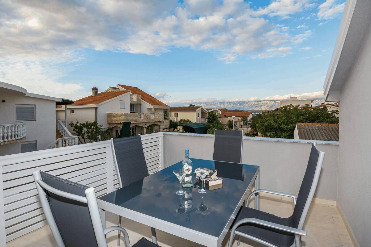 A balcony with a glass table, chairs, and a bottle of liquor.