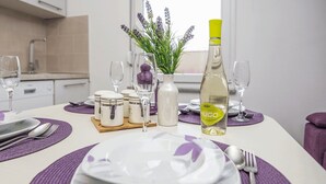 A neatly set dining table with white plates, purple placemats, and a bottle of HUGO wine. - Apartments Kosic (Vir)