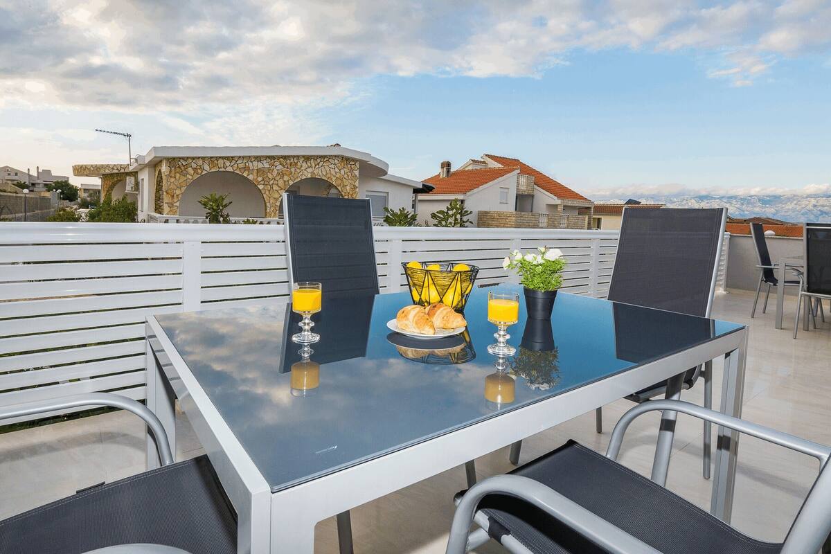 A rooftop terrace with a glass table, chairs, and a view of the cityscape.