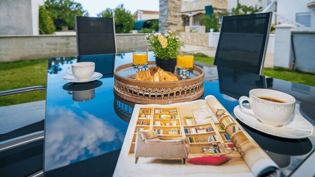 A breakfast setup on an outdoor table with a tray of croissants, two glasses of orange juice, a coffee cup, and a small potted plant. - Apartments Kosic (Vir)