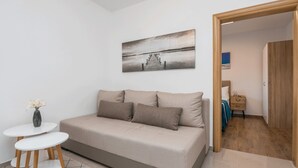 A modern living room with a sofa, a small table, and a painting of a pier. - Apartments Kosic (Vir)