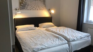Cama doble con cabecera, dos lámparas de noche y un cuadro con motivos playeros.