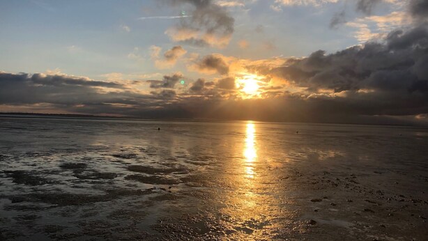 Un atardecer sobre una playa con cielo despejado y nubes.