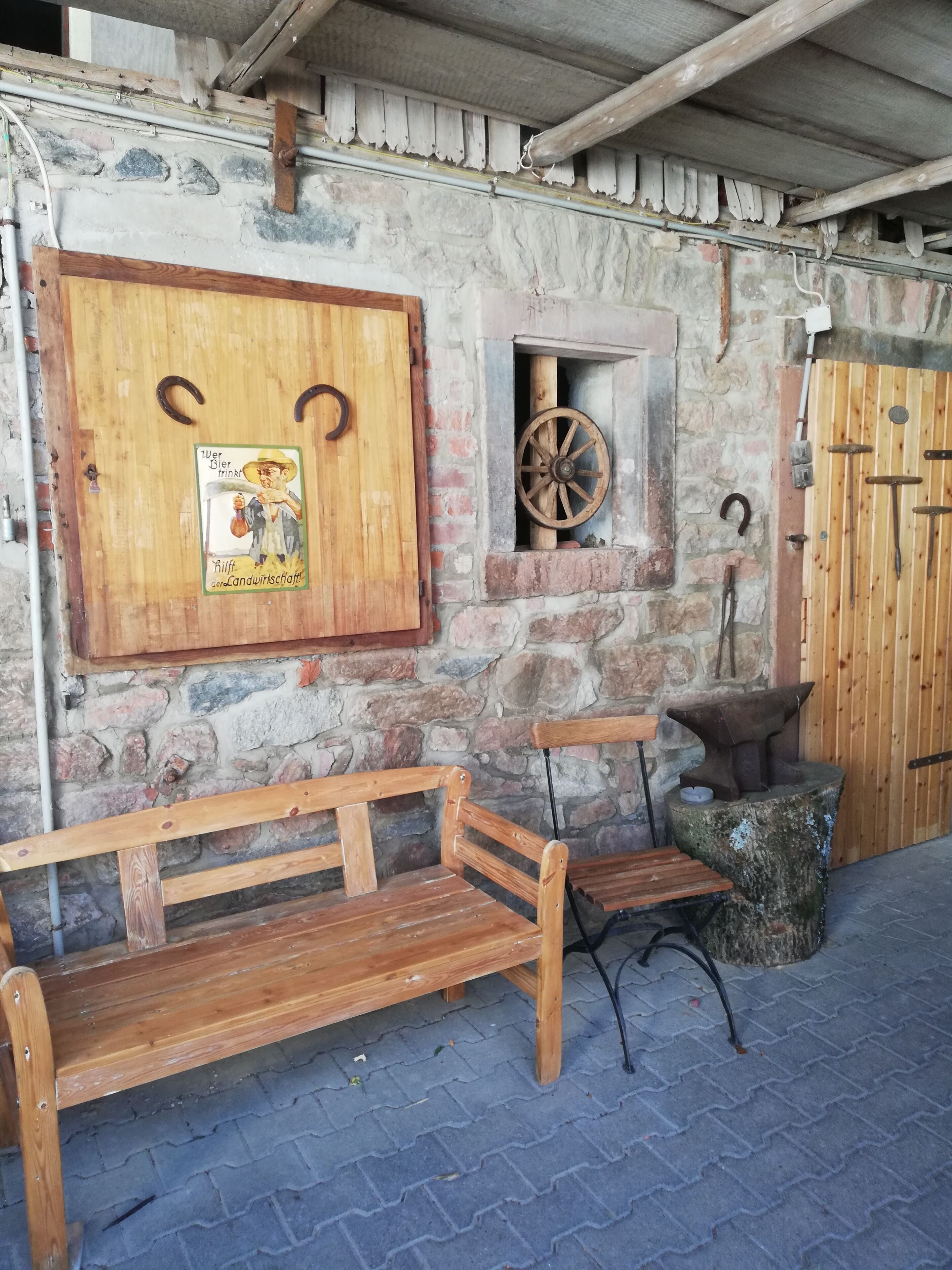 Un banco de madera rústico, un muro de piedra con una puerta de madera y un pequeño ventanal con una rueda de madera.