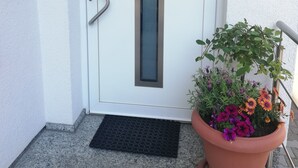 Een witte deur met een rechthoekig raam, een metalen handgreep en een zwarte mat bij de ingang.