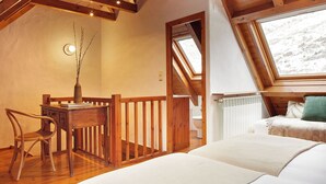 Une chambre confortable située dans les combles, avec un plafond en bois, un puits de lumière, un bureau avec une chaise et un lit agrémenté d’un oreiller vert.