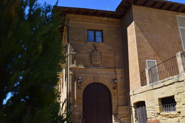 Un edificio de piedra con una puerta de madera grande, ventanas arqueadas y un pequeño balcón con barandilla.