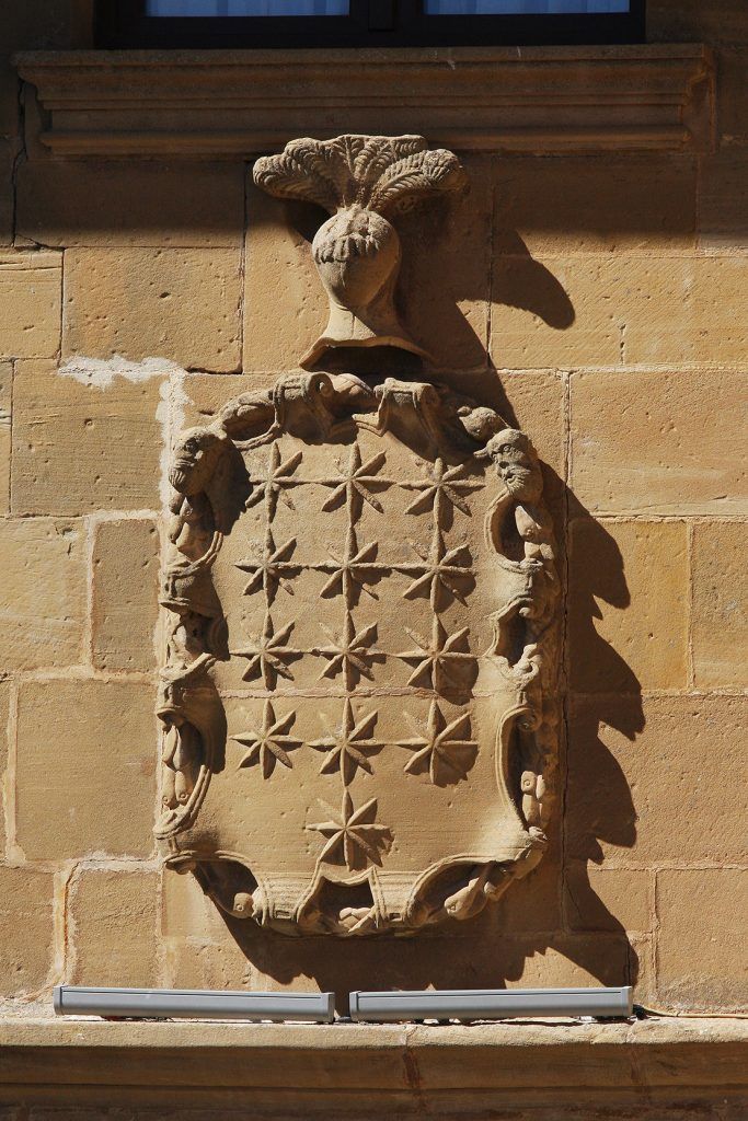 A stone wall with a carved emblem featuring a central figure and surrounding foliage.