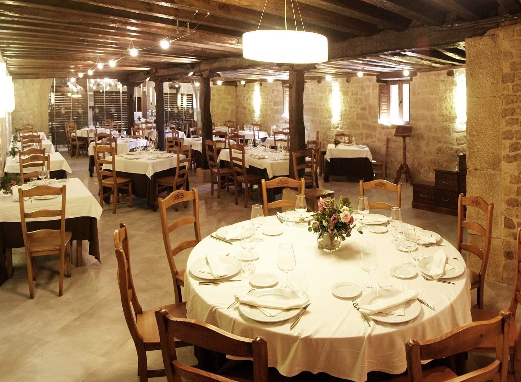 A restaurant with round tables set for dining, wooden chairs, and a chandelier.
