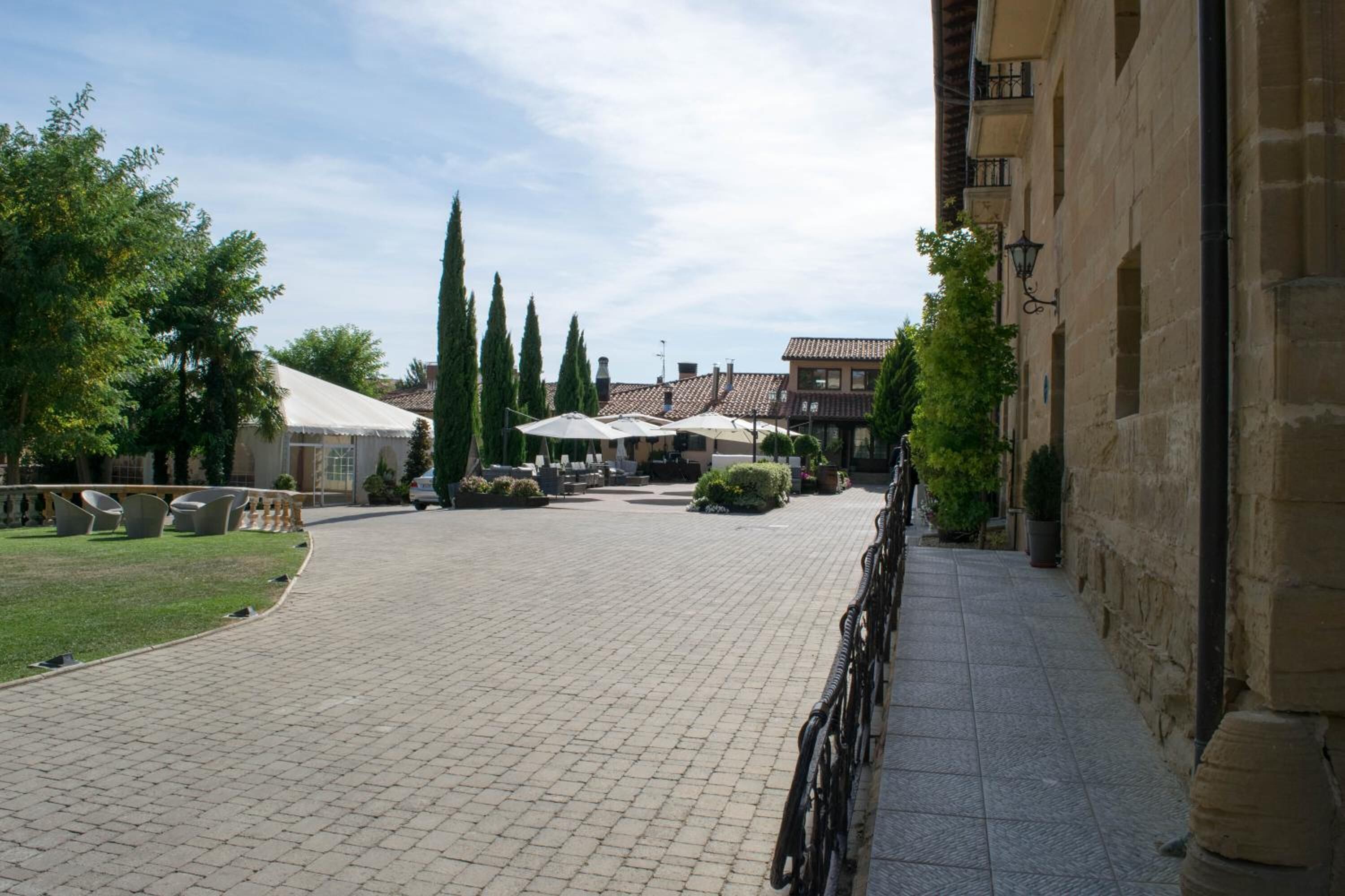 A paved courtyard with seating areas, a covered structure, and a building with a tiled roof.