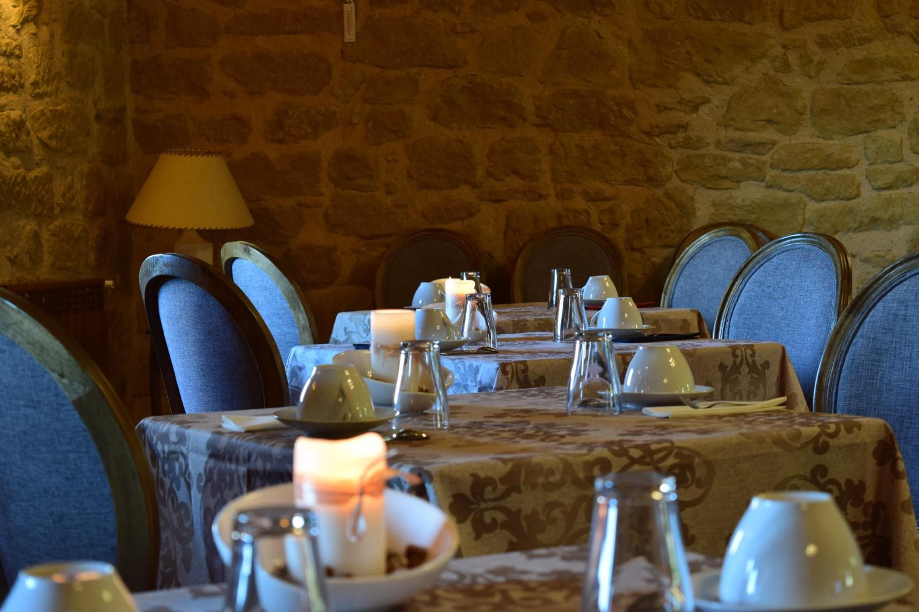 Una mesa de comedor dispuesta con tazas y platillos blancos, y una vela, rodeada de sillas tapizadas en azul.