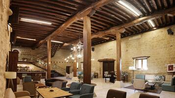 A spacious interior with high wooden beams, a chandelier, and a bar area with stools.