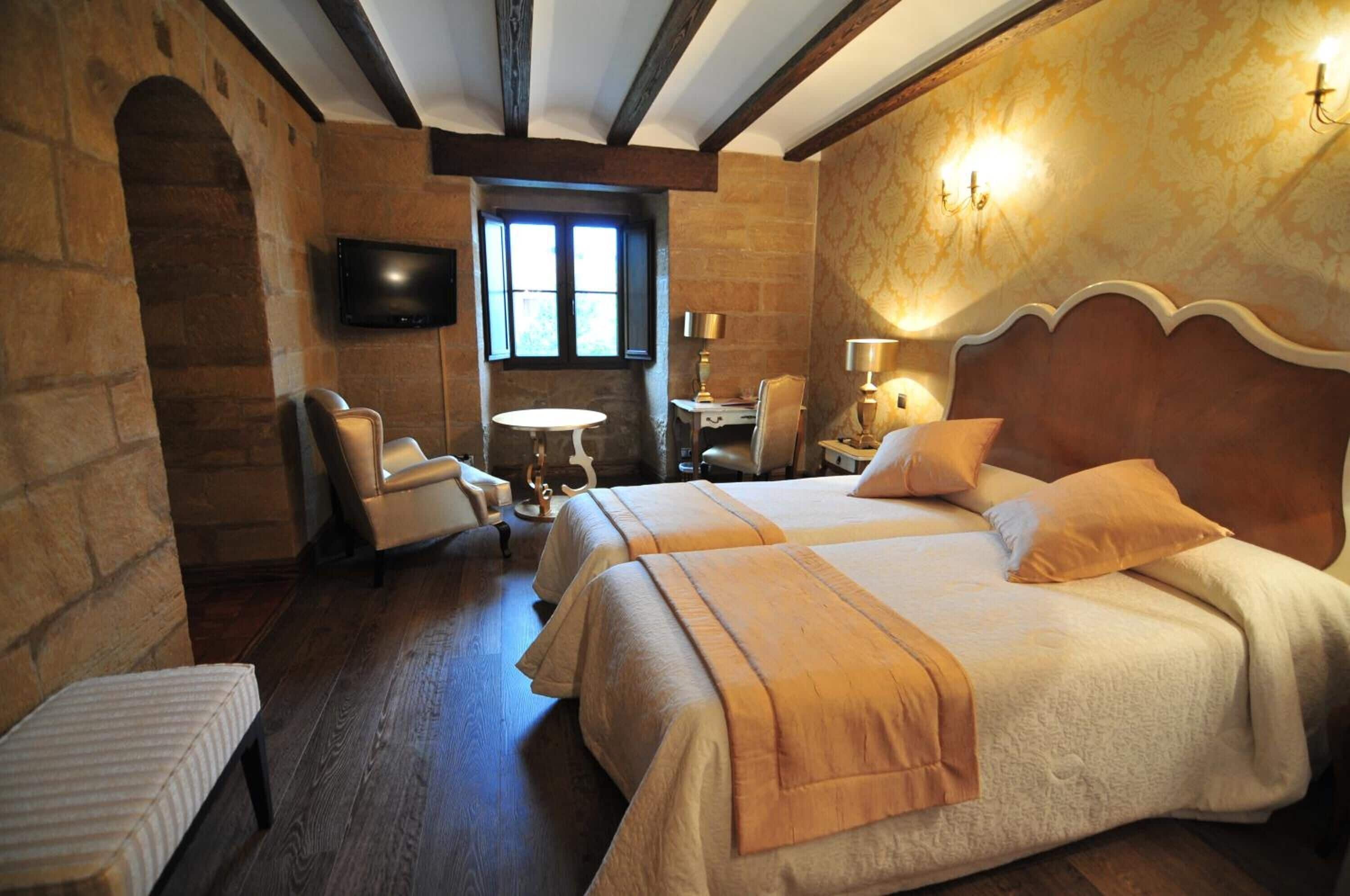 A hotel room with two beds, a TV, a small table, and a chair.