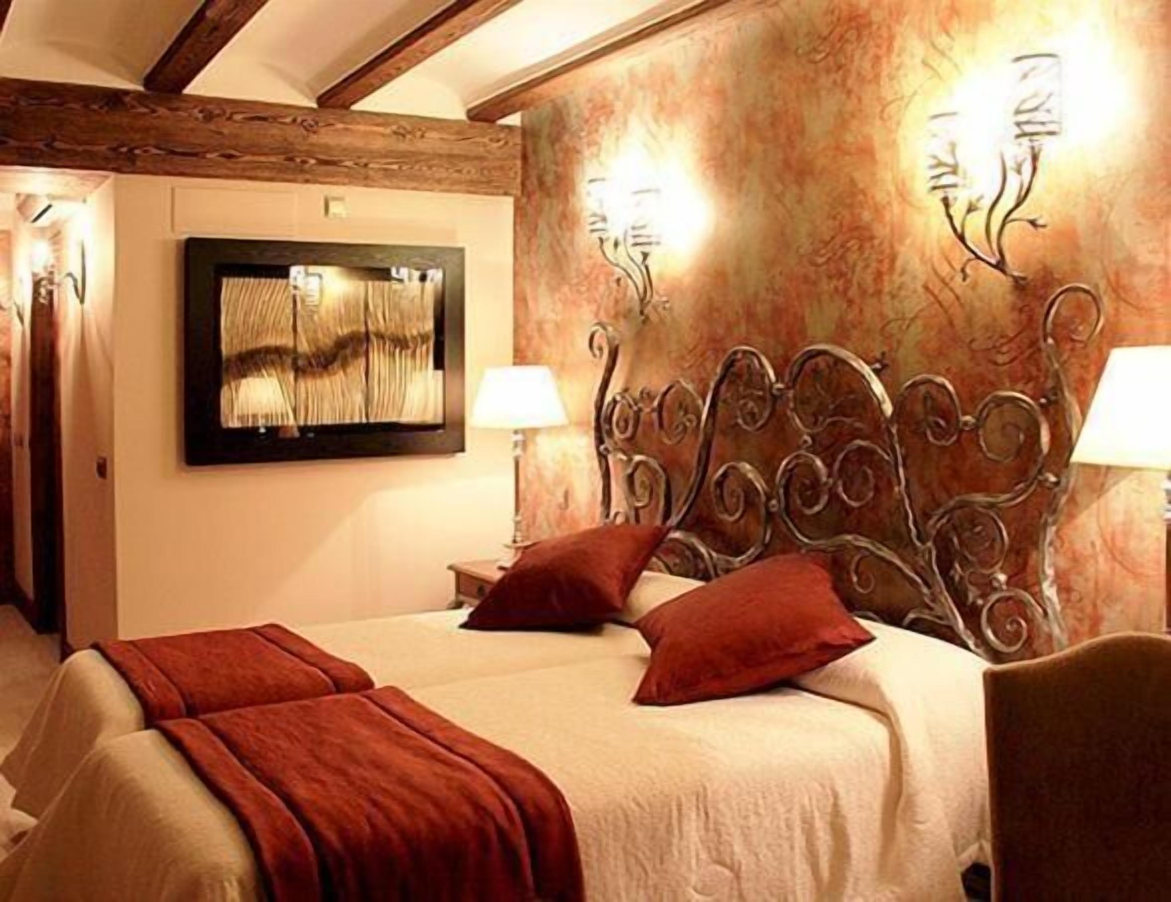 A hotel room with a bed, a television on the wall, and two wall-mounted lamps.