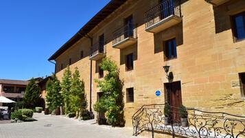 A traditional stone building with balconies, a paved courtyard, and potted plants.