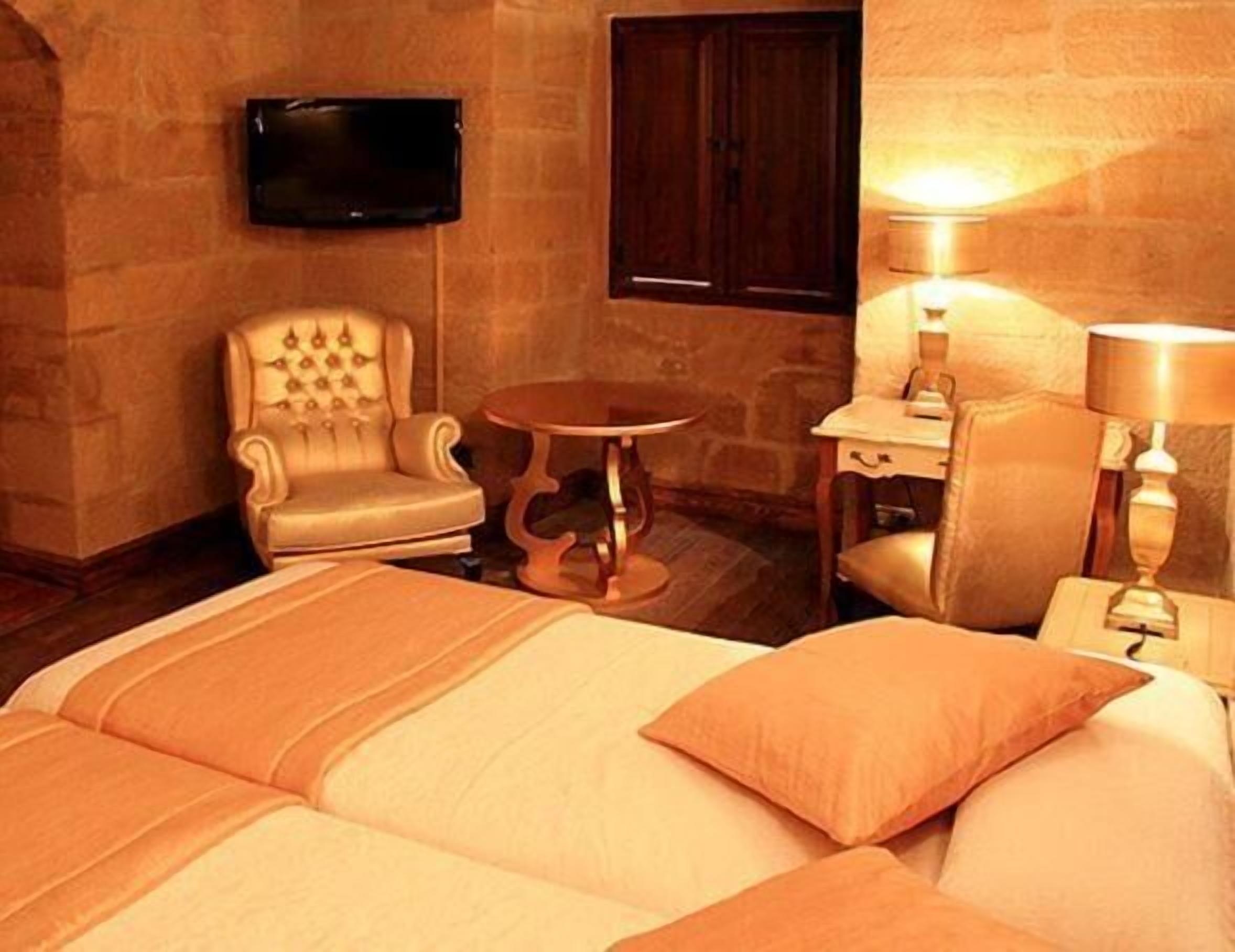 Habitación de hotel con cama, una silla, una mesita, televisor montado en la pared y lámpara en la mesita de noche.