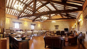 Une vaste salle dotée de poutres en bois et de murs en pierre, aménagée avec des tables et des chaises disposées pour les repas ou les moments de convivialité.