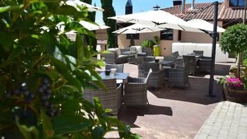 Un espace extérieur aménagé en terrasse, avec des meubles en osier, des parasols et des plantes en pot.