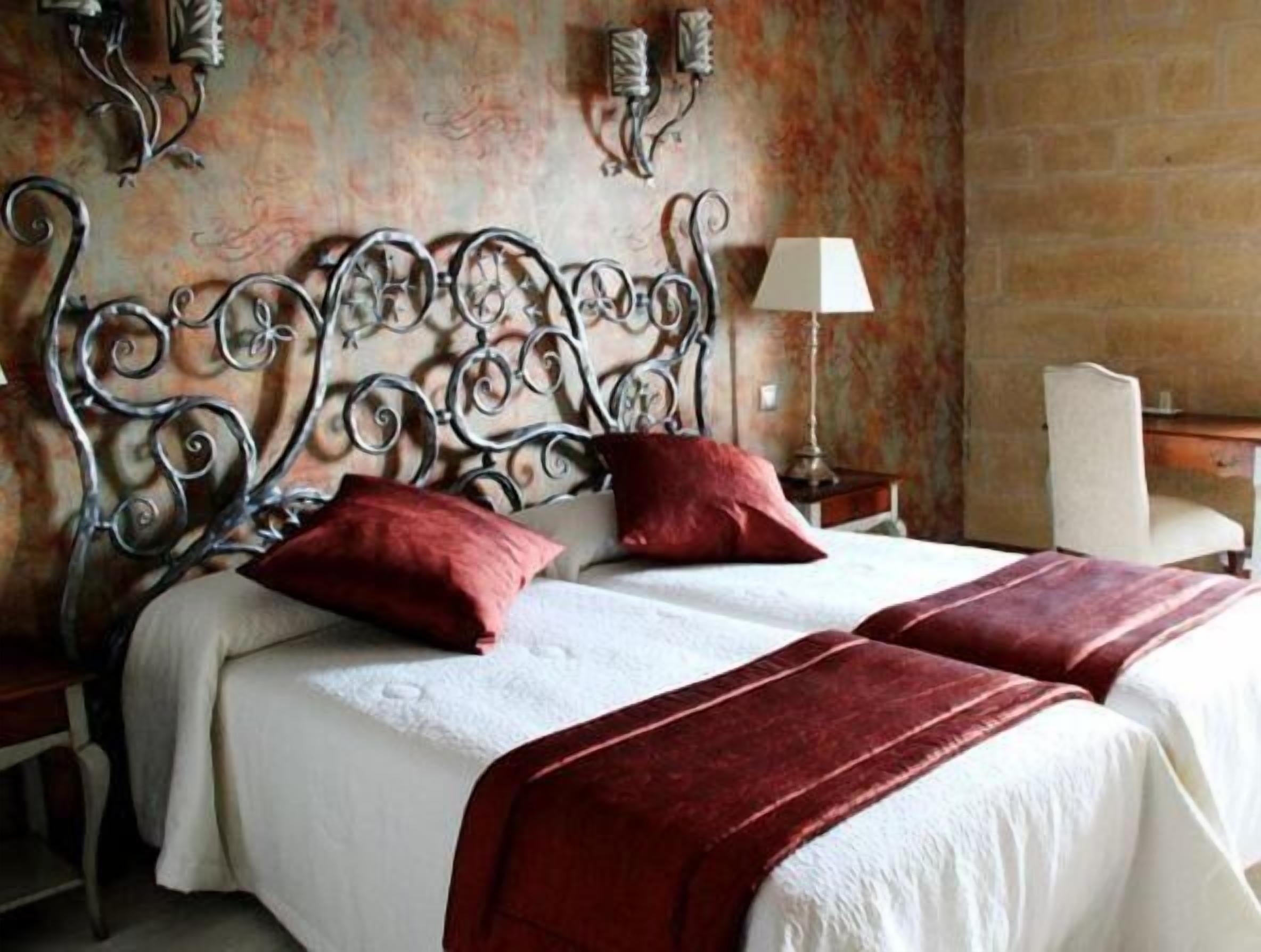 A double bed with a metal headboard, two red pillows, and a white bedspread.
