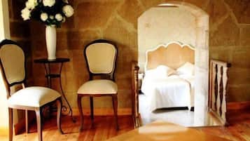 A bedroom with a bed, two chairs, a small table, and a vase of flowers.