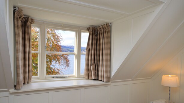 A room with a window overlooking a lake, a white lamp on a small table, and a white wall. - Darroch Beag Cottage, nearby Loch Fyne, peaceful location (St Catherines, Cairndow)