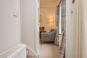 A narrow hallway leading to a bedroom with a bed, a bedside table, a lamp, and a window with curtains. - Darroch Beag Cottage, nearby Loch Fyne, peaceful location (St Catherines, Cairndow)