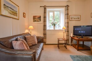 A furnished living room with a leather sofa, two lamps, a television, and framed pictures on the walls.