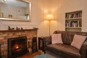 Una sala de estar acogedora con chimenea, sofá de cuero, estantería y lámpara.