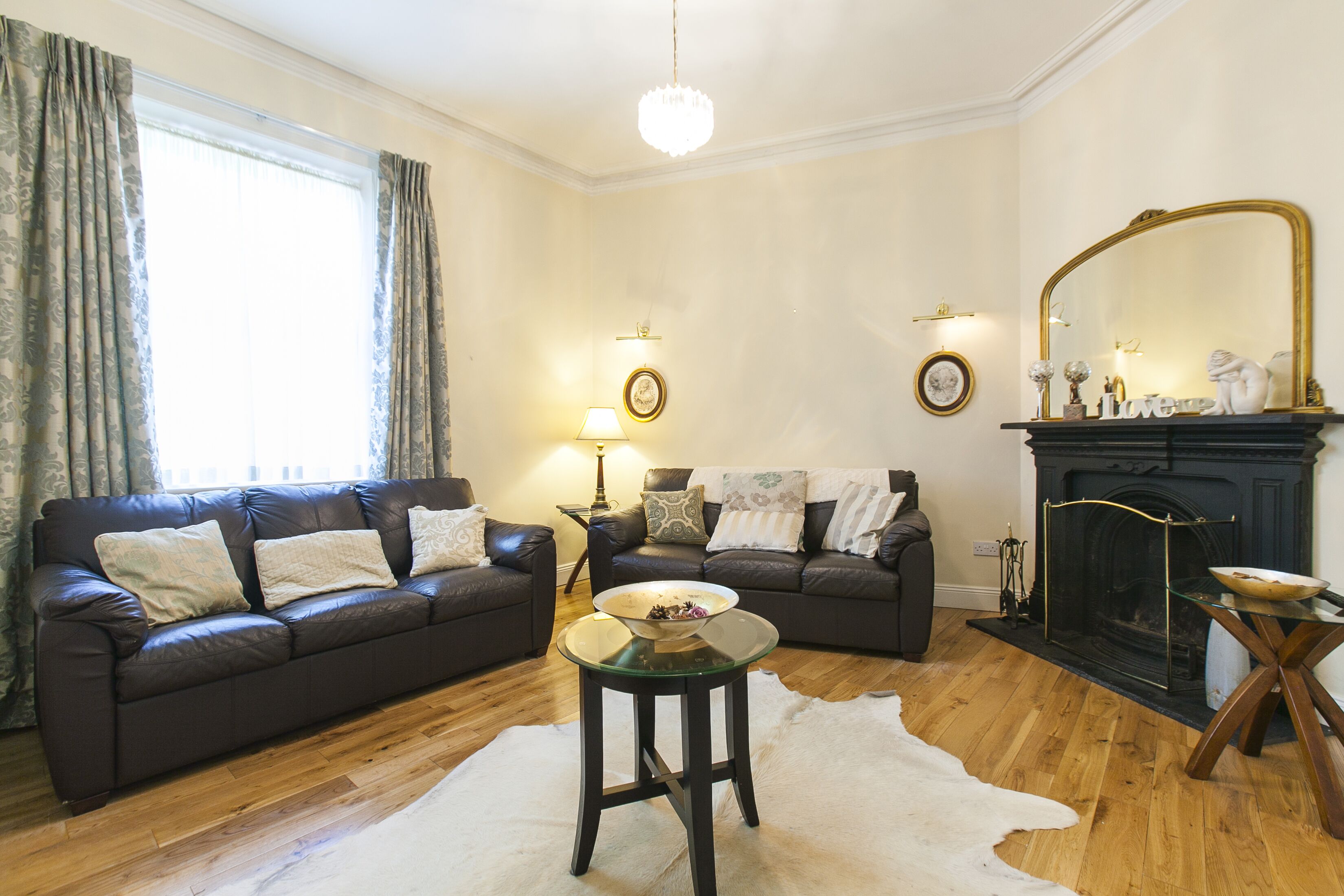 A living room with two dark brown sofas, a glass coffee table, a white rug, a fireplace, and a large mirror.