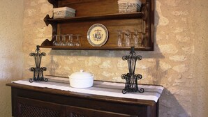 Une étagère en bois, sur laquelle sont posés des verres et un pot en céramique blanche, est fixée à un mur en pierre.