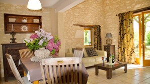 Un salon chaleureux avec une table à manger en bois, un canapé et une table basse. On peut voir un vase rempli de fleurs sur la table, et une lampe sur une table d’appoint.