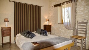 Une chambre à coucher avec un lit, deux tables de chevet avec des lampes, une chaise, une fenêtre avec des rideaux et un rideau à rayures à la fenêtre.