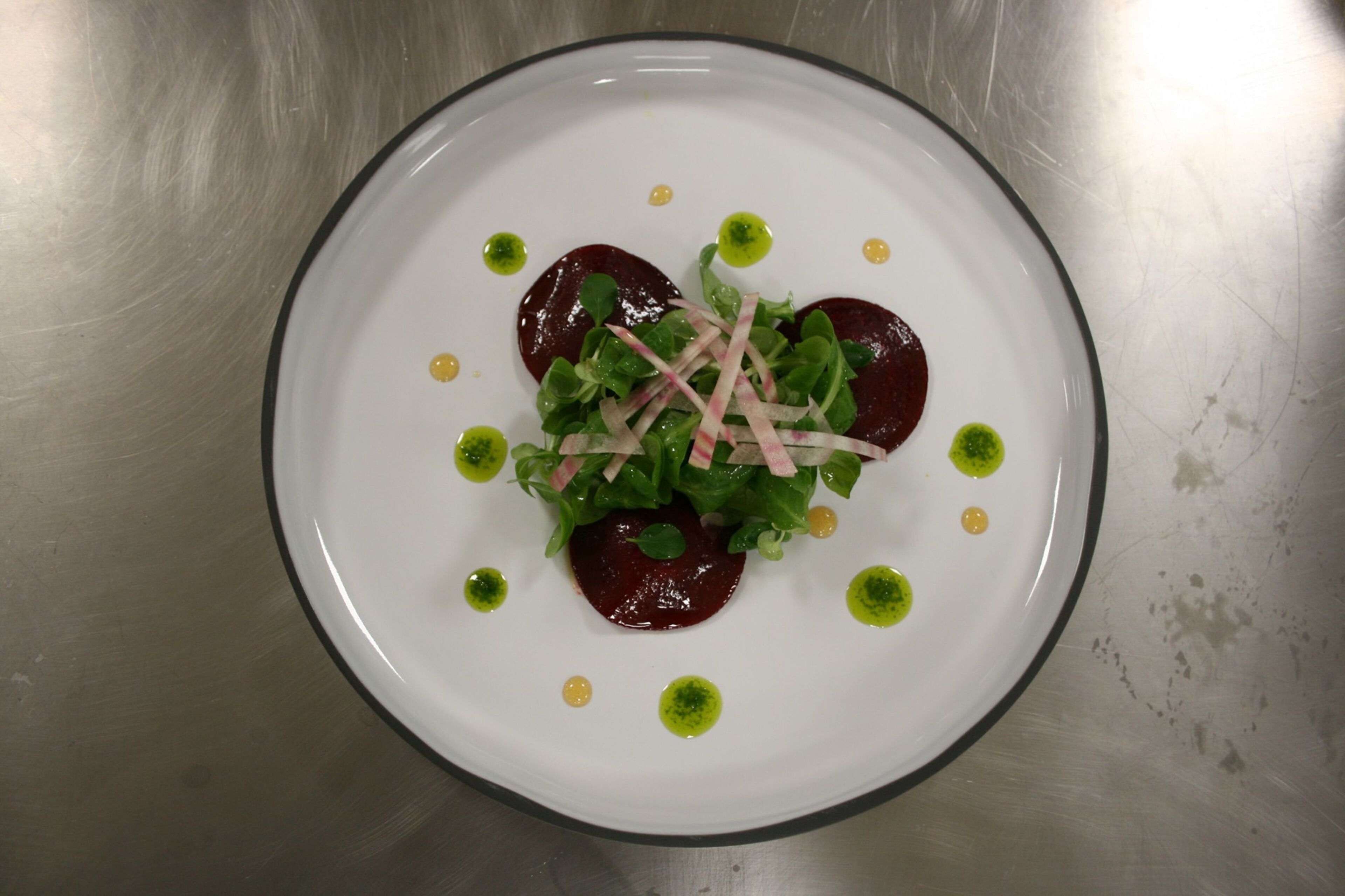 Un plato blanco con ensalada de remolacha, hojas verdes y pequeños puntos amarillos.