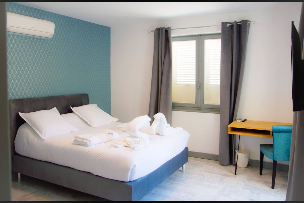 Una camera d'albergo con un letto, una scrivania, una sedia, una televisione e una finestra con tende.