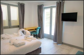 A hotel room with a bed, a desk, a chair, a TV, and curtains. - Hotel La Redonière (Romans-sur-Isere)