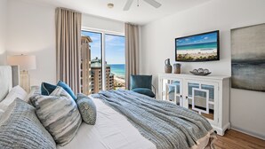 Ein Hotelzimmer mit Bett, Deckenventilator, Fernseher und Blick auf den Strand, sowie einem Schrank mit Dekorationen.
