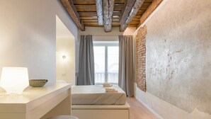 Une chambre à coucher avec un lit, une table de chevet avec une lampe, une fenêtre avec des rideaux et un mur en briques.