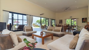 A spacious living room with a large window, a ceiling fan, and a dining area with chairs and a table. - Beachfront @ Lovina Beach, 8P, Private Pool, BBQ (Dencarik)