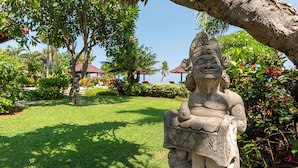 A statue in a garden with a clear sky, palm trees, and a building with a red roof in the background. - Beachfront @ Lovina Beach, 8P, Private Pool, BBQ (Dencarik)