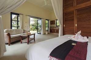 A bedroom with a large bed, a sofa, a small table, and a view of the outdoors through a sliding door.